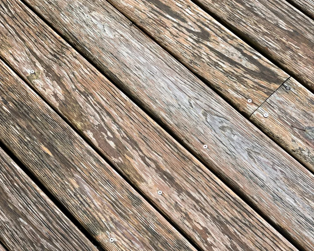Weathered grey deck boards laid diagonally, grain raised and checked