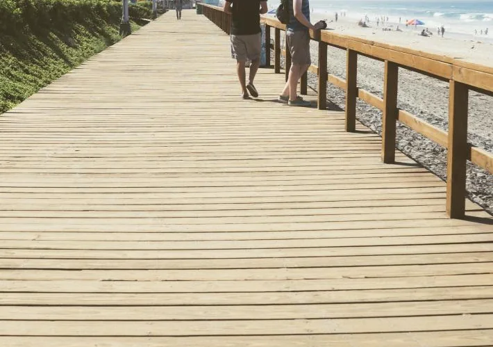 Wide timber boardwalk with a wooden rail running toward a beach