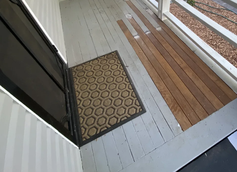 Narrow timber deck floor with a doormat beside a white balcony rail