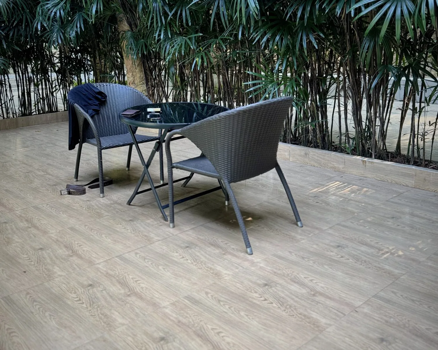 Small table and two chairs on a pale deck against a screen of tall planting