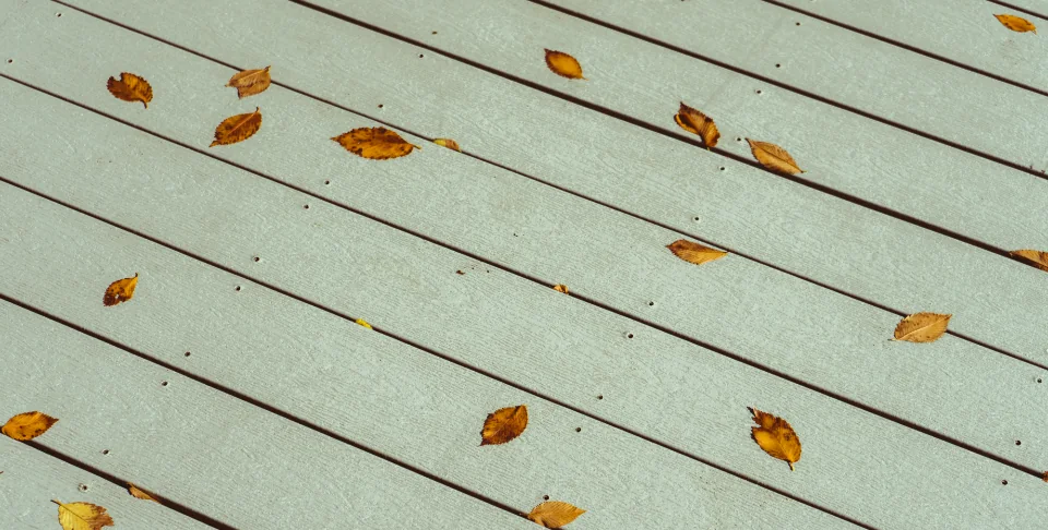 Pale grey composite deck boards with a few fallen leaves across them